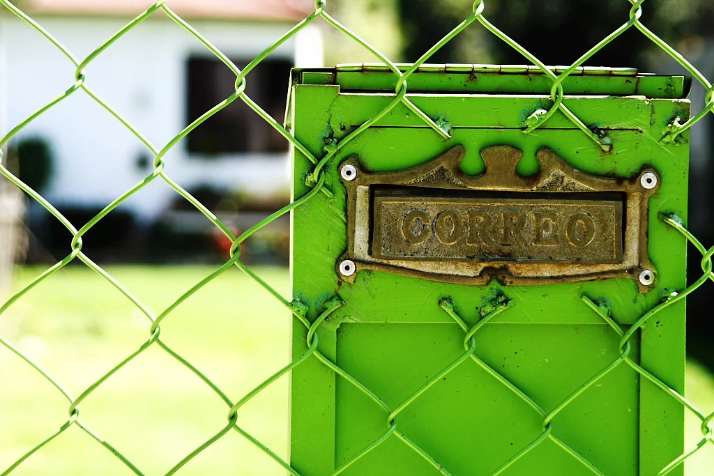 Green metal mailbox behind a chain-link fence