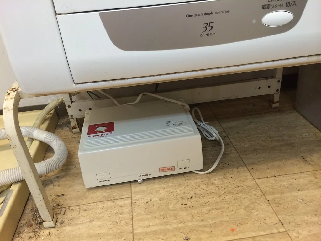 White Wi-Fi router sitting on the floor under a washing machine